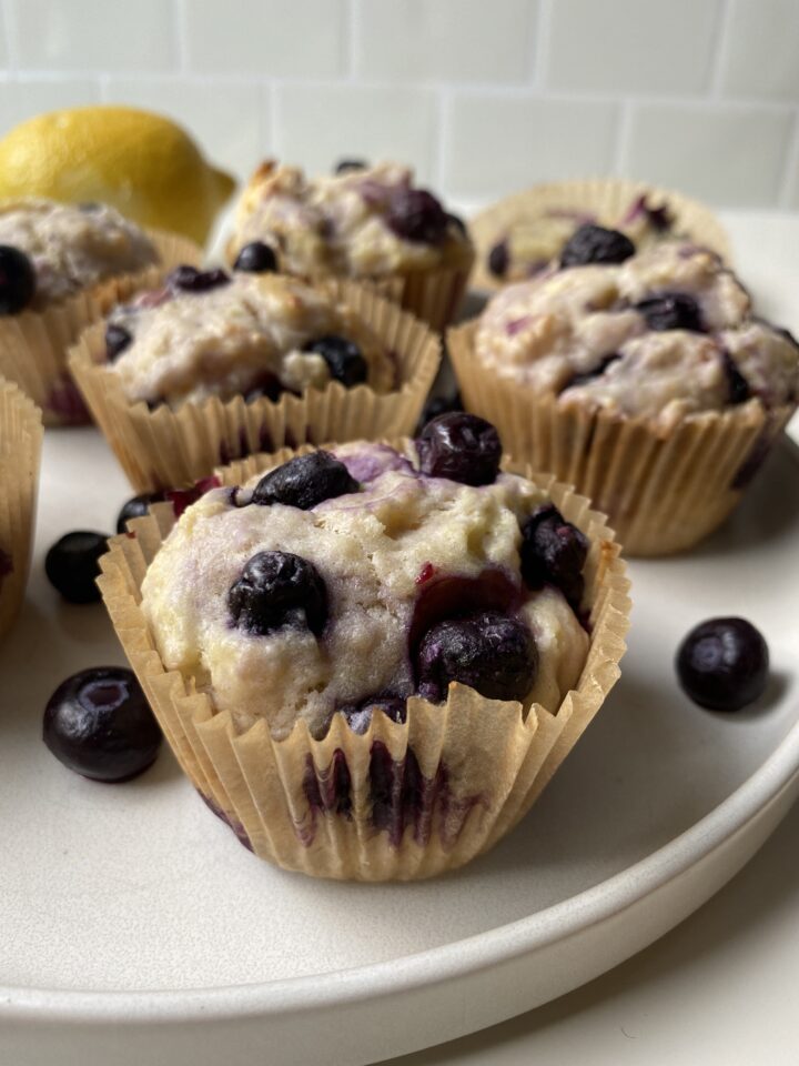 Close up of one gluten free lemon blueberry muffin on a plate with some blueberries on the side