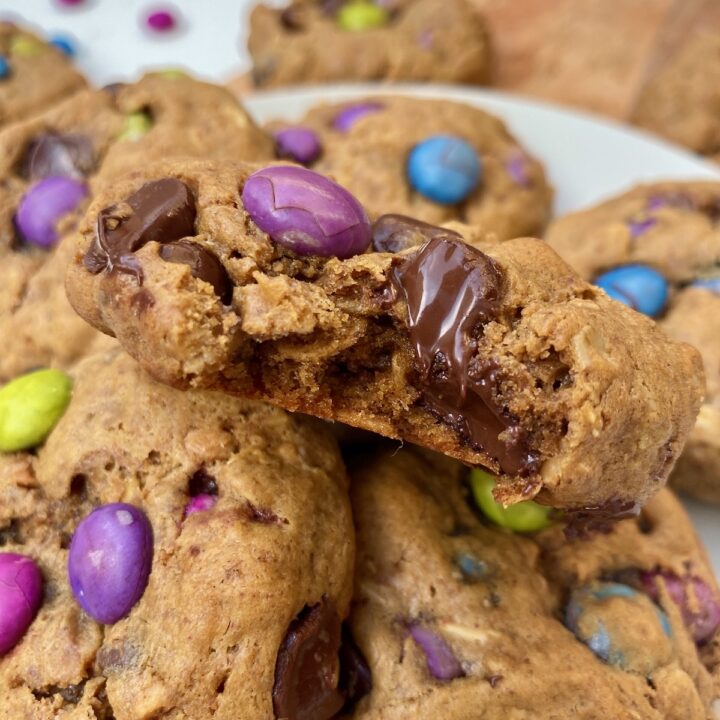 close up of some gluten free monster cookies. the one on top is bitten into and chocolate is oozing out of it