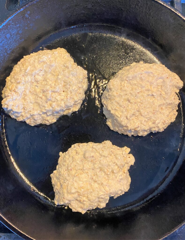 3 Vegan banana pancakes cooking in a cast iron skillet, before flipping