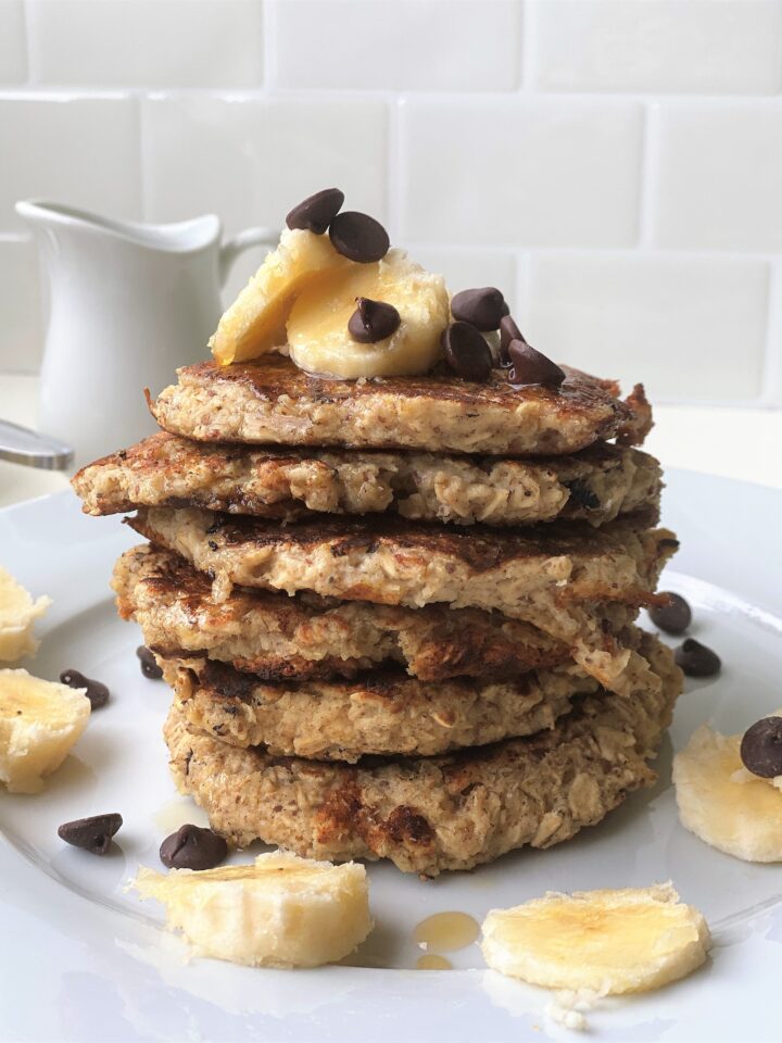 Stack of 6 vegan banana pancakes on a plate with a white backsplash in the background