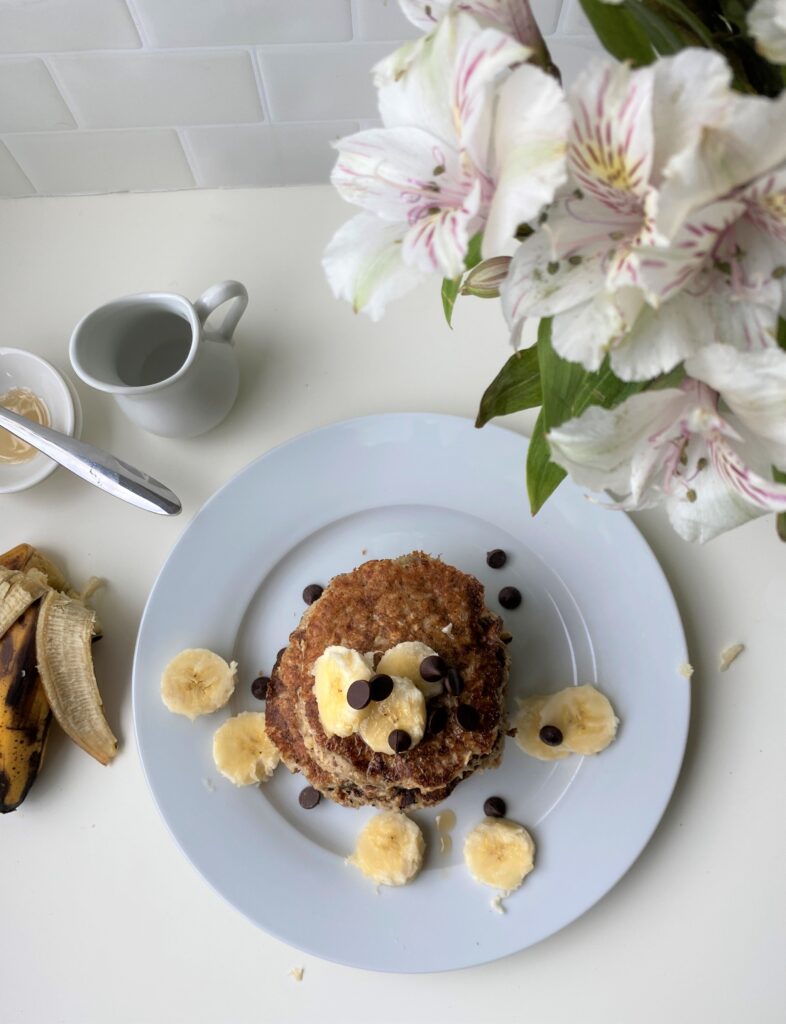 Bird eye view shot of stacked banana pancakes, with flowers and small milk jar